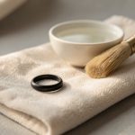 Bague en argent noirci ornée d’une pierre naturelle, posée sur un chiffon doux avec de l’eau tiède et une petite brosse pour un nettoyage délicat.
