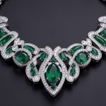Collier contemporain de haute joaillerie en platine, orné d’émeraudes et de diamants brillants sur un fond sombre raffiné.